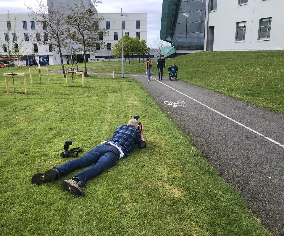 Picture of man lying down taking picture of 3 people in ATU Galway city campus
